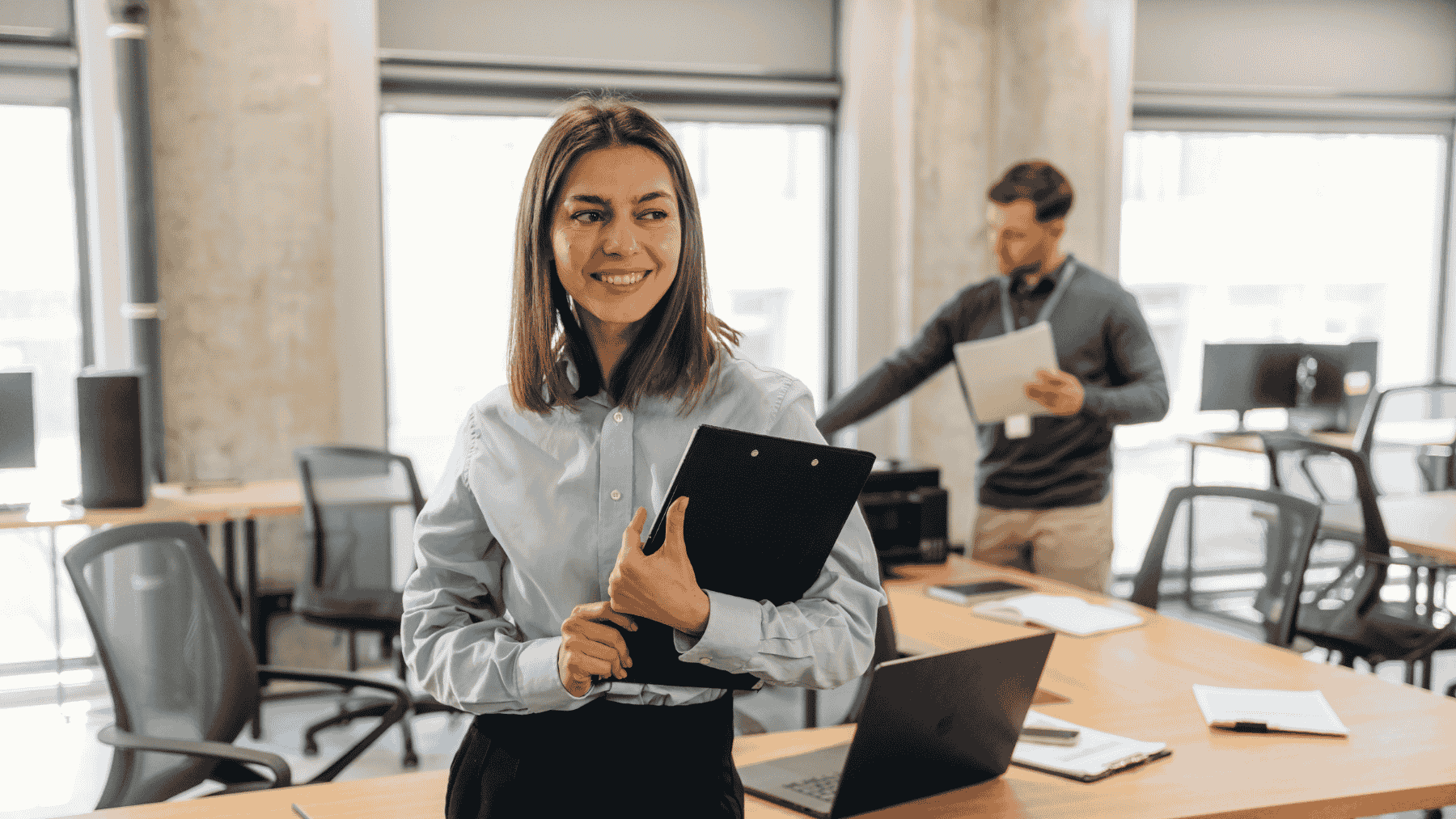 femeie tanara ce sta cu laptopul in brate intr-un birou